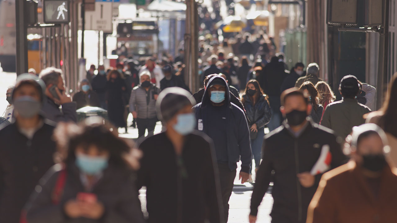 Crowd of people walking street wearing masks